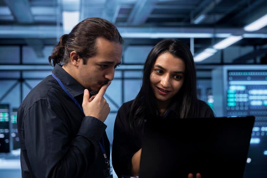 IT professionals collaborating on a laptop in a server hub, discussing data protection strategies and innovative IT solutions.