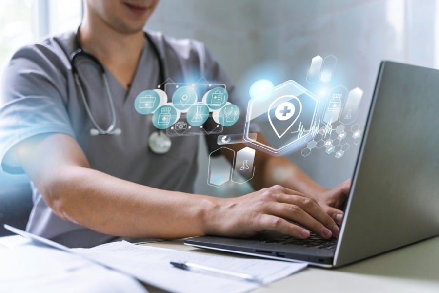 Doctor in scrubs using a laptop with digital health icons, symbolizing secure transfer of medical information and HIPAA compliance.
