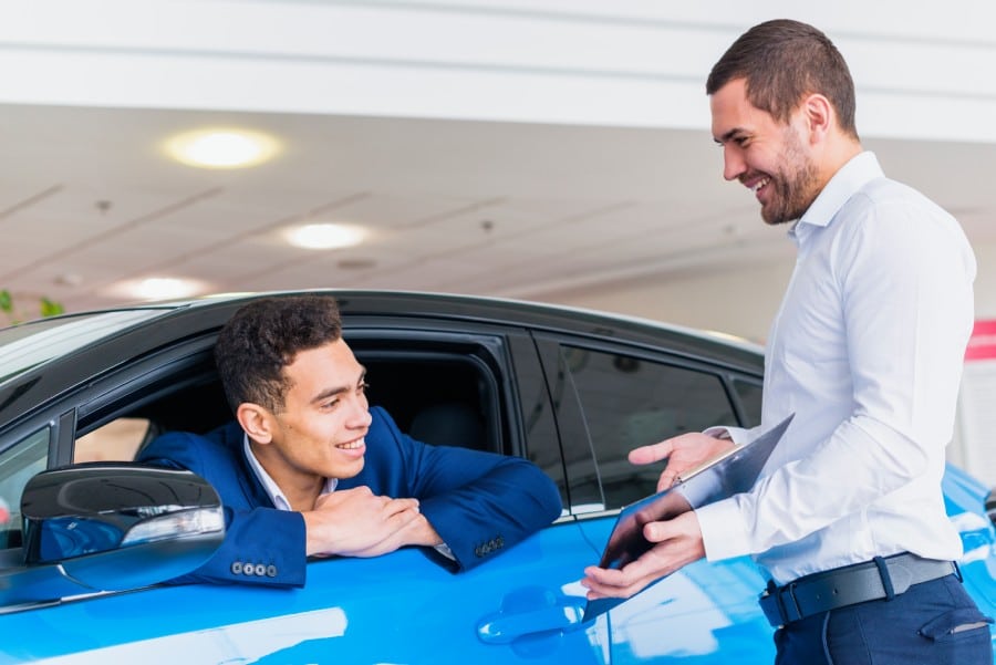 Salesman assisting customer in car dealership, discussing vehicle options and services.