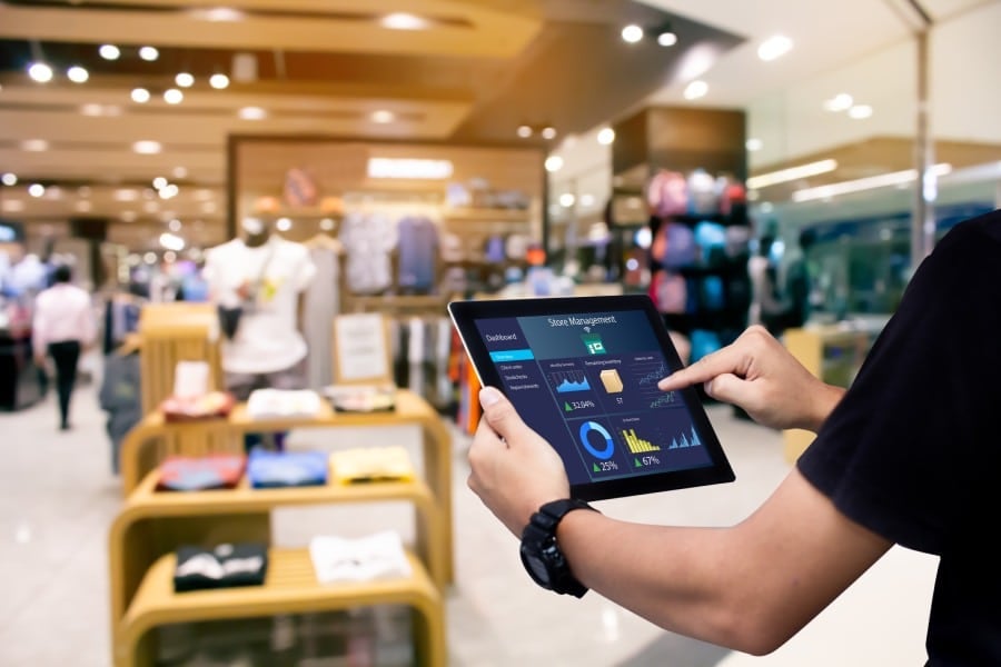 Person using a digital tablet displaying store management dashboard in a retail environment, showcasing technology integration for streamlined store operations.
